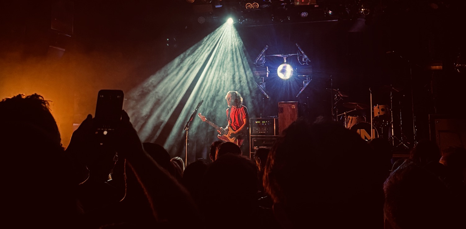 A guitar player playing in a nightclub surrounded by smoke