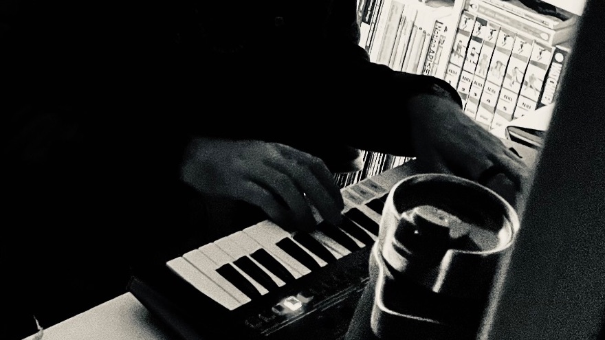 A black and white photo of a small keyboard synth with hands playing it